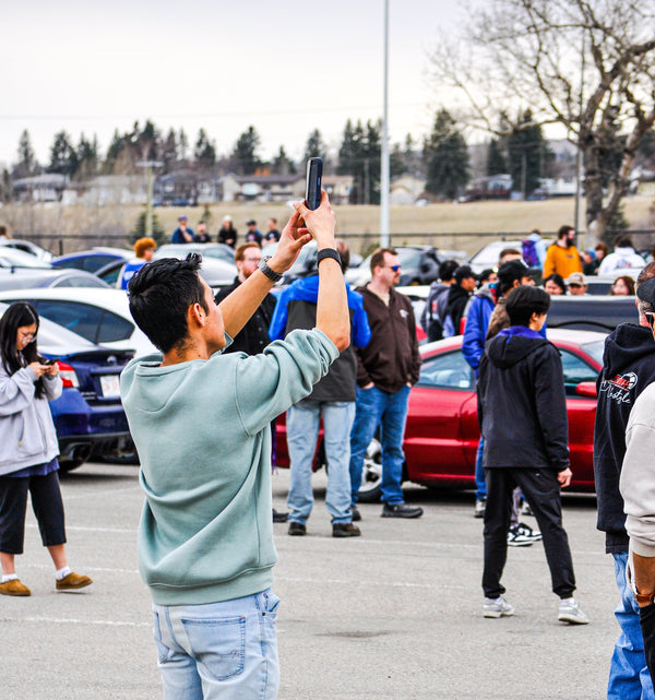 Person taking a photo with a smartphone in a parking lot with other people and cars.