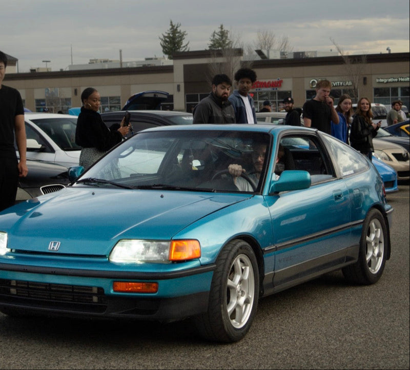 Blue Honda car with people around it in a parking lot